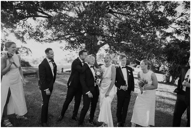 Ella & Jackson at The Woods: The groom and wedding party laugh together outdoors.