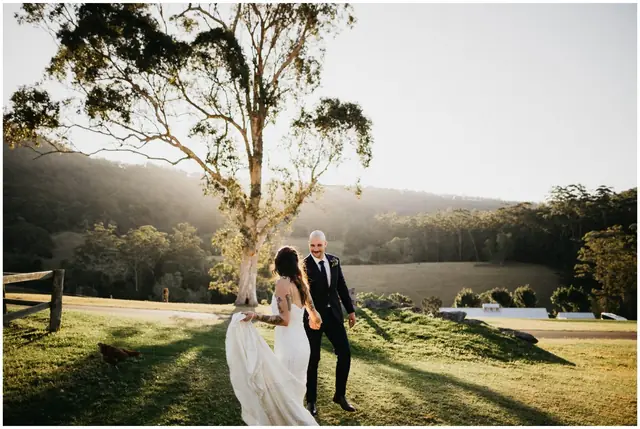 Luke & Cara at Cowbell Creek: The couple walk towards a large tree in a green paddock.