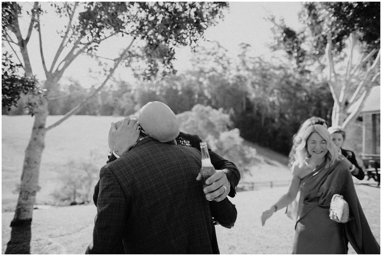 Luke & Cara at Cowbell Creek: The groom embraces a guest outdoors.