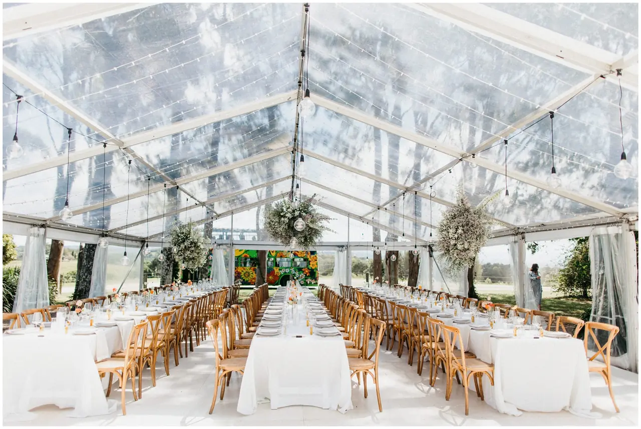 Marty & Nicola at Byron View Farm: Long reception tables beneath a clear marquee and hanging lights.