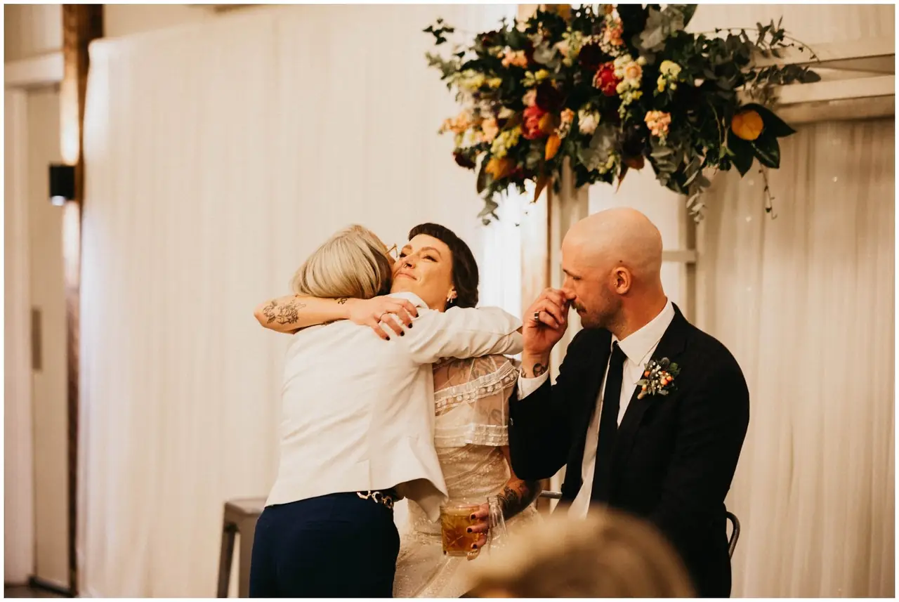 Luke & Cara at Cowbell Creek: The bride embraces a guest beside the seated groom.