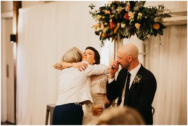 Luke & Cara at Cowbell Creek: The bride embraces a guest beside the seated groom.