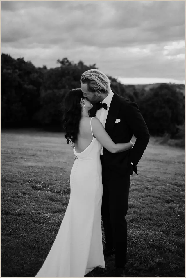 Jess & Rich at The Orchard Estate: The couple share a kiss in a paddock beneath a cloudy sky.