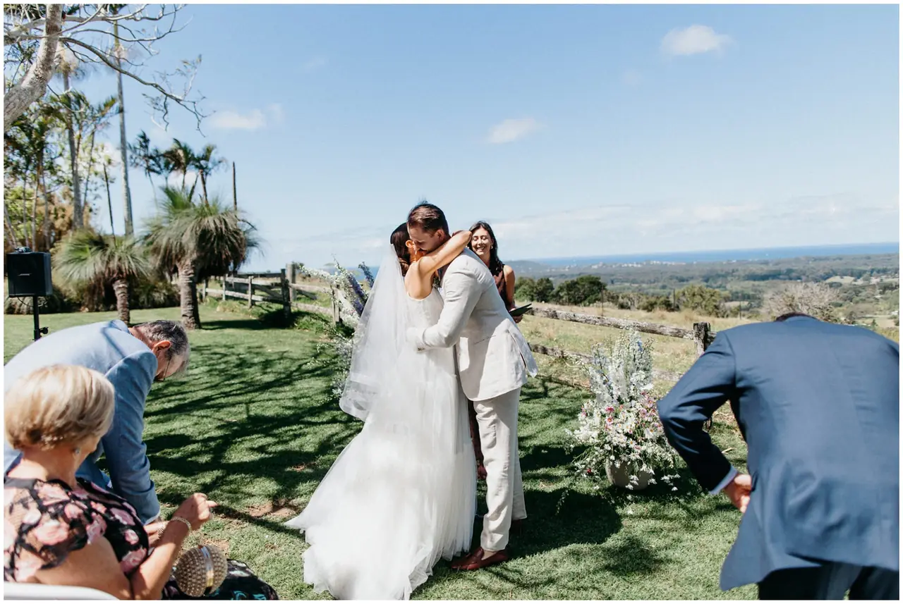 Marty & Nicola at Byron View Farm: The couple embrace after the ceremony with the coastline in the distance.