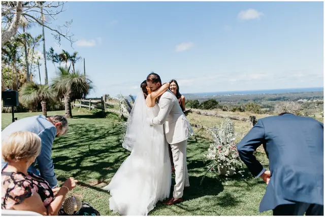 Marty & Nicola at Byron View Farm: The couple embrace after the ceremony with the coastline in the distance.