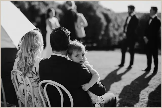 Jess & Rich at The Orchard Estate: A guest holds a small child during the outdoor ceremony.
